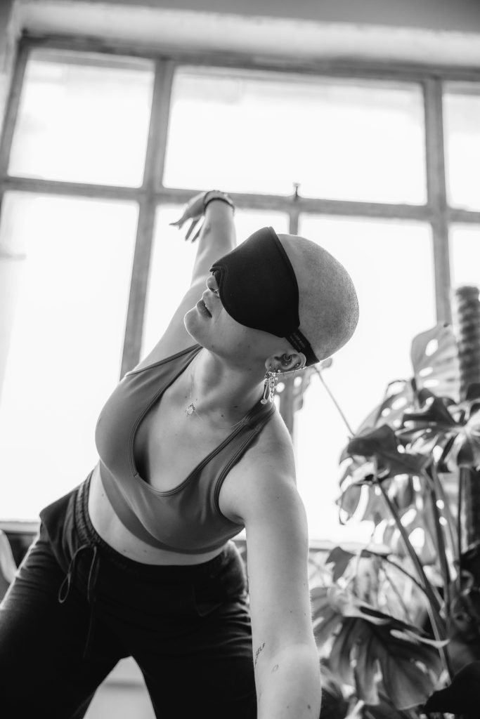 bald woman in a yoga studio with an eye mask, plants, pilates ball, yoga blanket, yoga strap - black and white