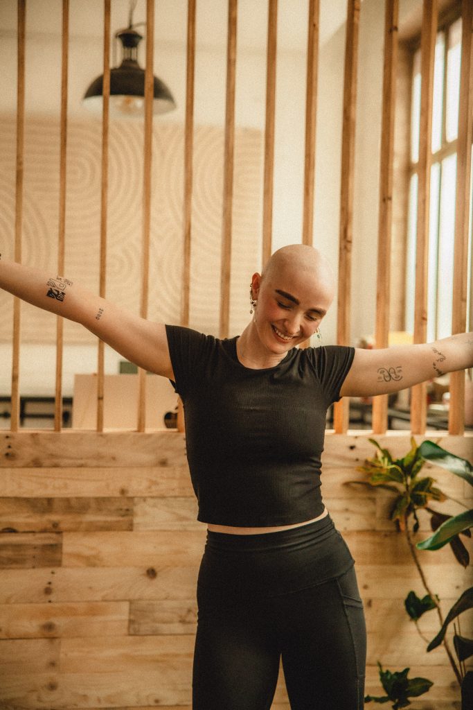 bald woman dancing in a yoga studio, plants, pilates ball, yoga blanket, yoga strap