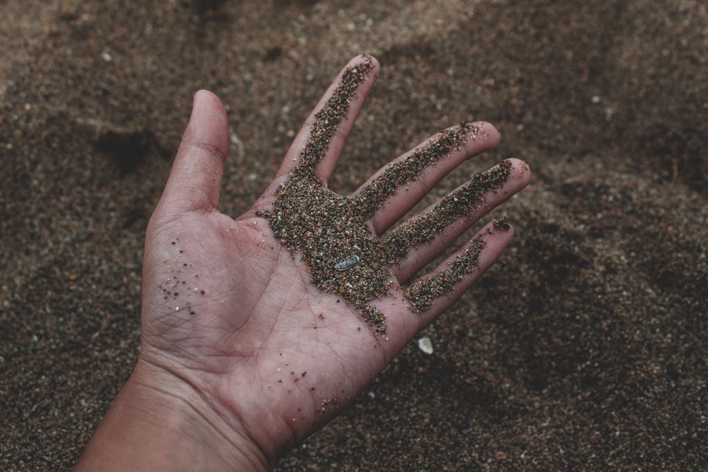 A close-up photo of a hand holding damp sand, showing texture and natural detail.