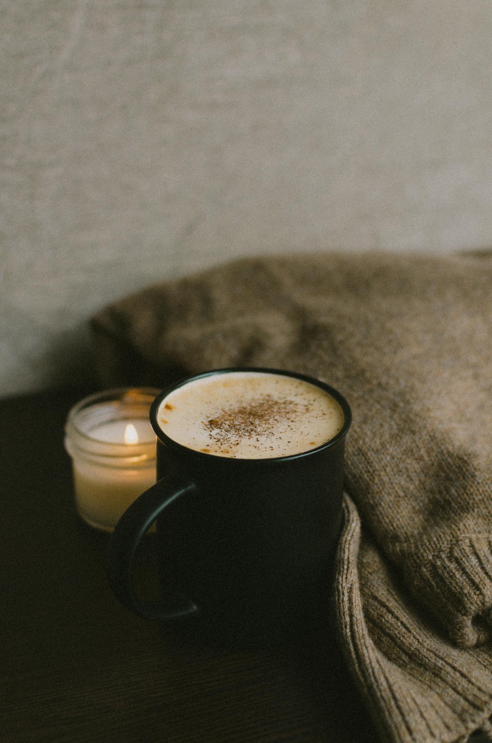 A warm, cozy setup with a cup of coffee and a candle resting on a sweater.