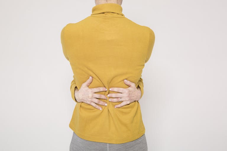 Man in a yellow sweater posing creatively by hugging himself in a studio setting.