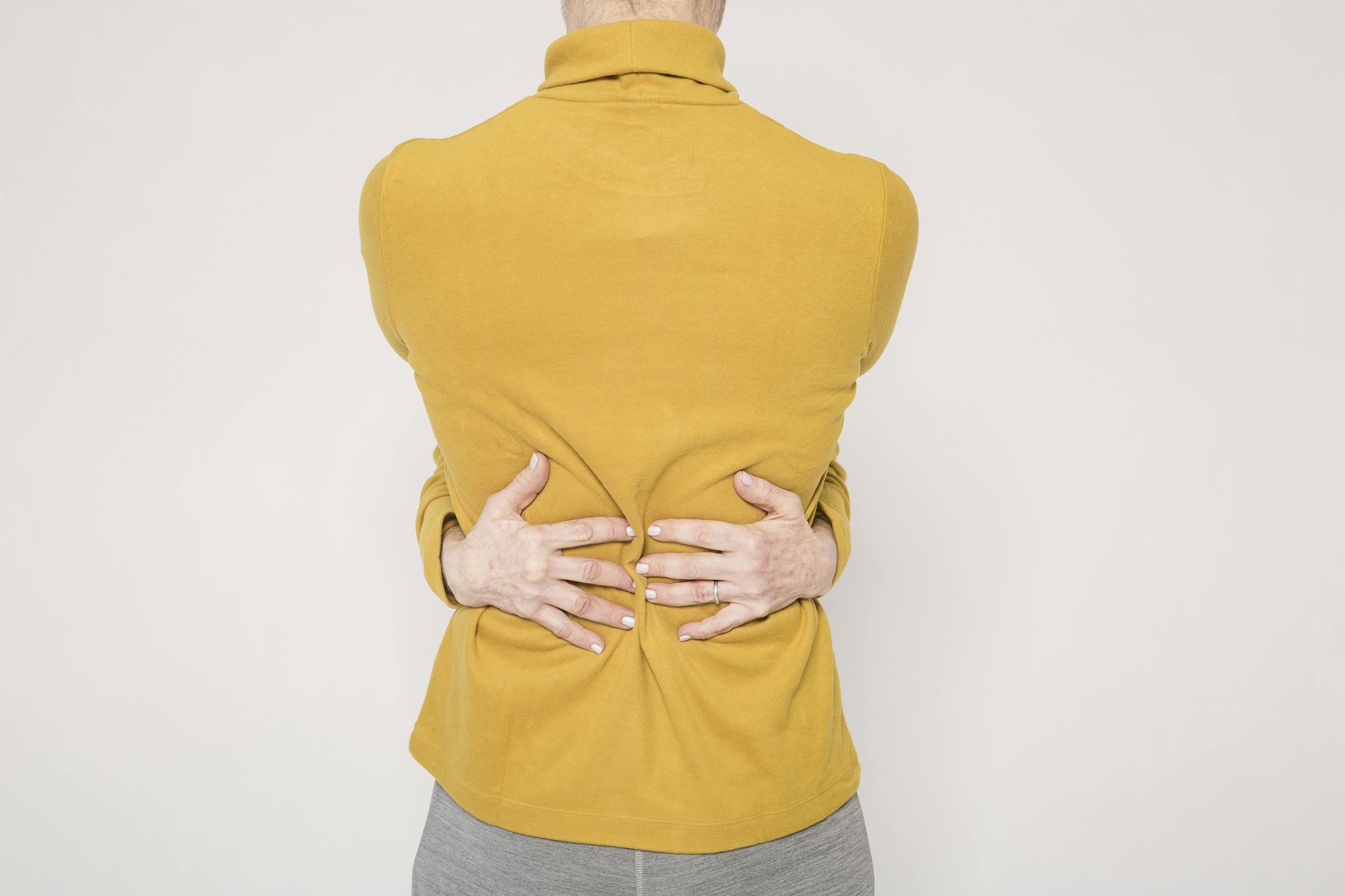 Man in a yellow sweater posing creatively by hugging himself in a studio setting.